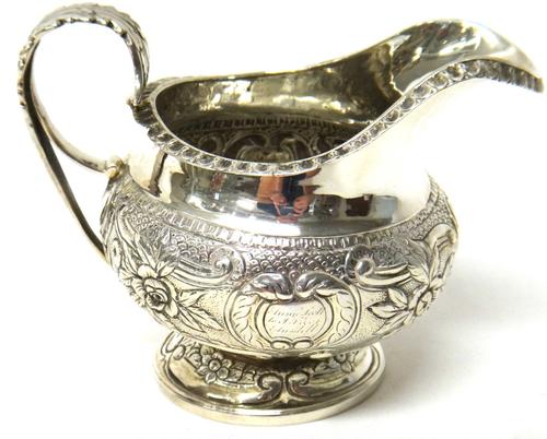 A George III silver milk jug, with floral, foliate and scroll embossed decoration, with a foliate capped handle and on a circular foot, London 1816, w