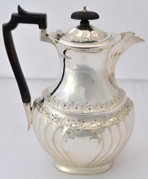 A late Victorian silver hot water jug, of oval baluster form, decorated with spiral bands and with floral and foliate rims, with ebonised fittings, Sh