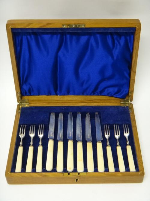 A set of six pairs of silver dessert  or fruit knives and forks, with silver blades and prongs and with ivory handles, Birmingham 1928, with an oak ca