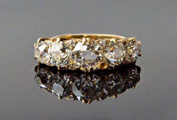 A gold and diamond five stone ring, circa 1900, mounted with a row of cushion shaped diamonds, graduating in size to the centre stone and with pairs o