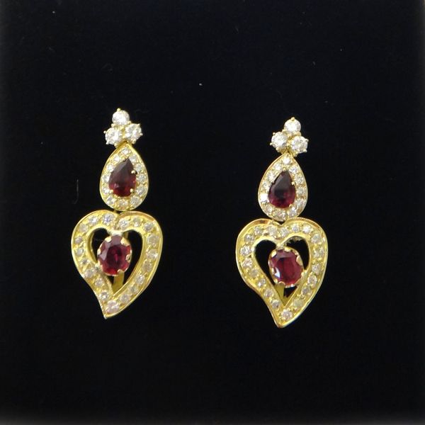 A pair of gold, ruby and diamond pendant earrings, each drop mounted with an oval cut ruby to the centre, within a heart shaped surround, mounted with