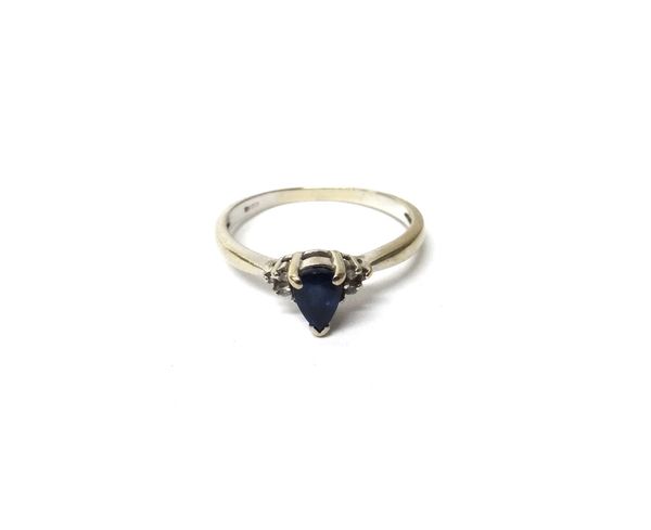 A white gold, sapphire and diamond ring, claw set with the pear shaped sapphire at the centre, between circular cut diamond set three stone shoulders,