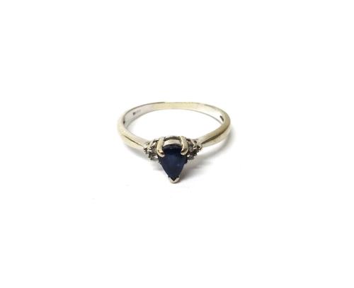A white gold, sapphire and diamond ring, claw set with the pear shaped sapphire at the centre, between circular cut diamond set three stone shoulders,