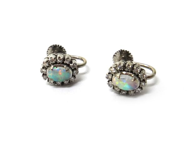 A pair of opal and diamond set oval cluster earstuds, each claw set with the oval opal at the centre within a surround of circular cut diamonds, the b