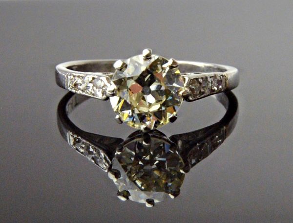 A platinum and diamond ring, claw set with the principal circular cut diamond at the centre, between diamond set three stone shoulders, detailed PLAT,