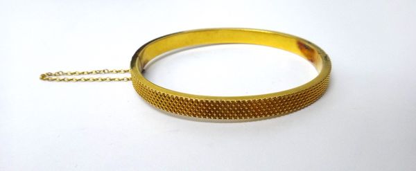 A gold oval hinged bangle, the back and the front with cross hatched decoration, on a snap clasp, fitted with a safety chain, gross weight 8.8 gms.