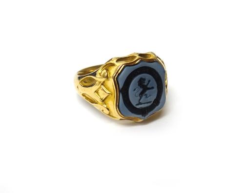 A gold and banded agate set shield shaped signet ring, crest and motto seal engraved, between decorated shoulders, ring size N., gross weight 7.1 gms.