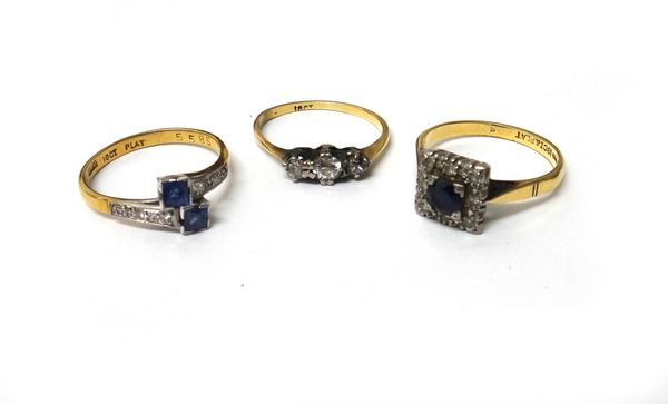 A gold and diamond three stone ring, claw set with cushion shaped diamonds, a gold and platinum, sapphire and diamond set nine stone square cluster ri