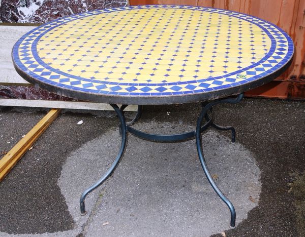 A yellow and blue mosaic tile inset circular garden table, on a metal base, 121cm diameter.  OUT