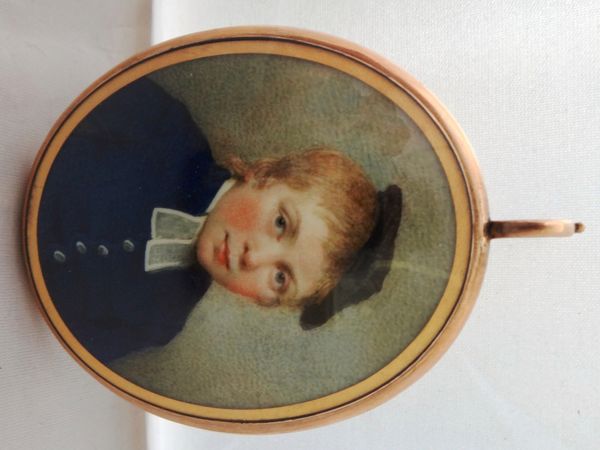 An early 19th century English school portrait miniature on ivory of a young boy in blue coat with large white buttons and wearing a cap, reverse glaze