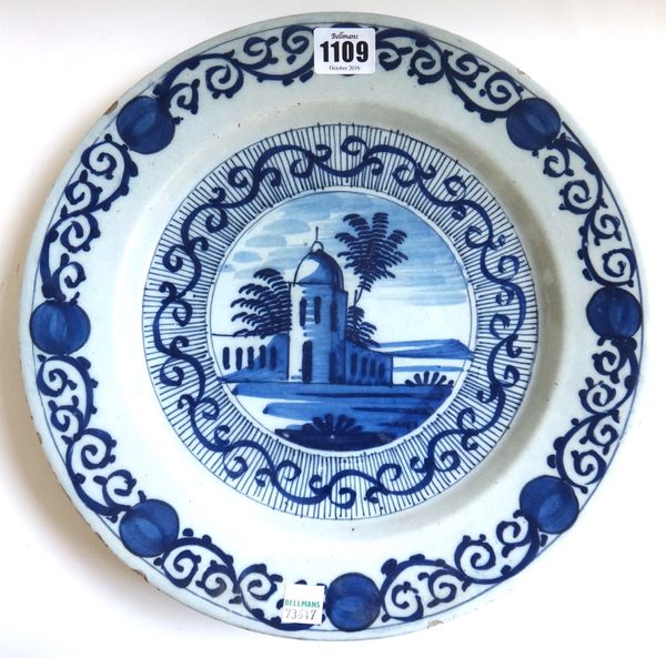 An 18th century Dutch Delft plate, decorated in tones of blue, with a central temple scene, within a wide scroll border, 30.5cm diameter.