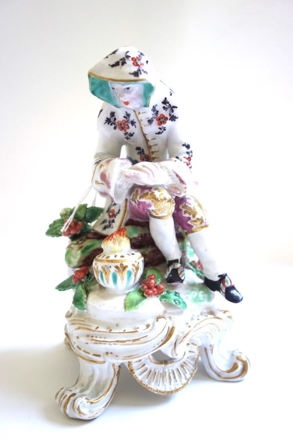 A Bow figure of Winter, circa 1765, modelled as a seated man warming his hands over a brazier, raised on a scroll moulded base picked out in gilding,