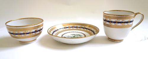 A Derby porcelain trio, circa 1785, painted with pattern 86, a landscape vignette inside blue and gilt borders, crossed batons and 'D' marks and patte