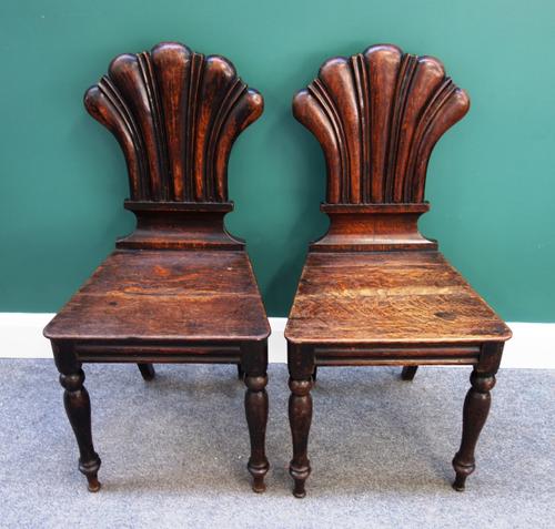 A pair of 19th century oak hall chairs, each with stylised shell back and solid seat, on baluster turned supports (2).