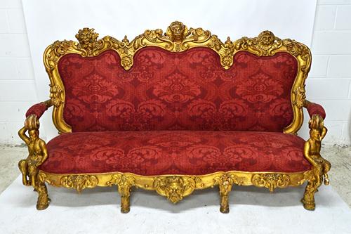 In the manner of Brustolon; a mid-19th century Italian gilt framed sofa carved with grotesque masks amongst fruiting vines, the open arms on seated Pa