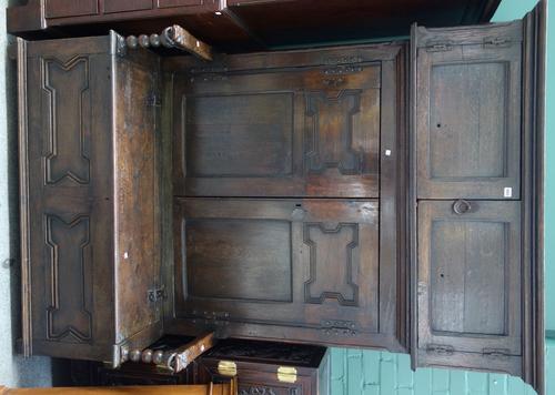 A 17th century and later made-up oak bacon cupboard/settle, with two pairs of cupboard doors over lift top seat, mounted with grotesque arm finials, 1