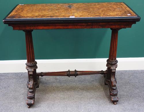 A Victorian burr walnut card table, the rectangular fold over top on a pair of fluted columns united by stretcher, on four scroll supports, 92cm wide.