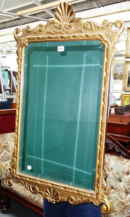 An early 18th century style gilt framed pier glass, with shell carved upper and lower frieze about the shaped bevelled mirror plate, 61cm wide x 100cm