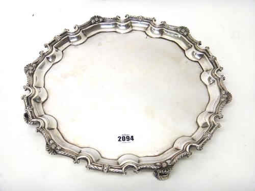 A silver salver, the shaped Chippendale style pie-crust rim further enhanced with a cast border, having scalloped motifs, raised on four scrolling fee