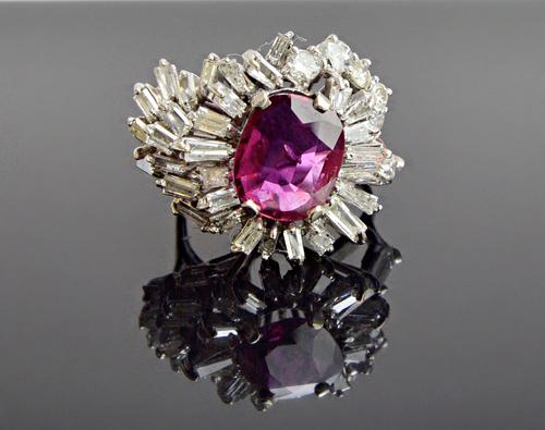 A magenta sapphire and diamond set cluster ring, claw set with the oval cut cushion shaped magenta sapphire at the centre, in a surround of baguette a