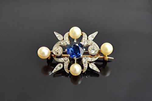 A sapphire, diamond and cultured pearl brooch, claw set with the circular cut sapphire to the centre, between the two principal cushion shaped diamond