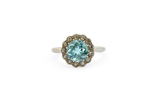 A white gold and platinum, blue zircon and diamond set cluster ring, claw set with the circular cut blue zircon at the centre, within a surround of sm