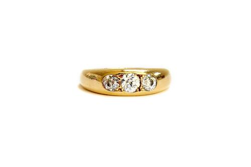 A gold and diamond set three stone ring, gypsy set with a row of cushion shaped diamonds and with the principal diamond mounted at the centre, ring si