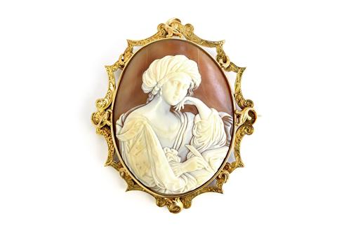 A Victorian gold mounted oval shell cameo brooch, carved as the figure of a lady writing with a plume, the gold mount with scroll engraved decoration,