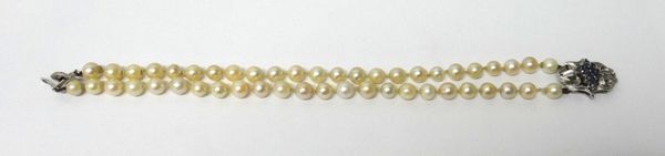 A two row bracelet of uniform cultured pearls, on a white gold and sapphire set clasp of foliate design, the centre mounted with a lozenge shaped clus