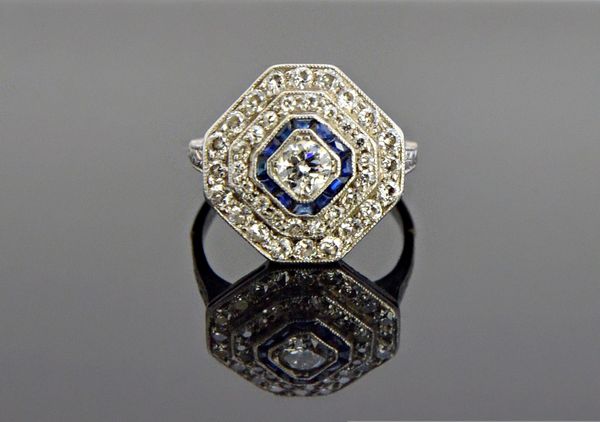 A diamond and blue gem set octagonal shaped cluster ring, mounted with the principal circular cut diamond at the centre, in a calibre cut blue gem set