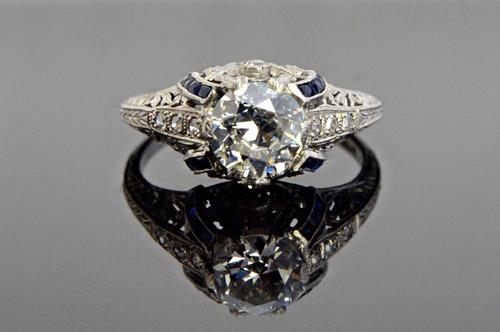 A platinum, diamond and sapphire set ring, mounted with the principal cushion shaped diamond at the centre, between diamond set three stone shoulders