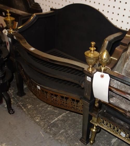 A serpentine iron steel and brass fire grate with urn finials. DISPLAY