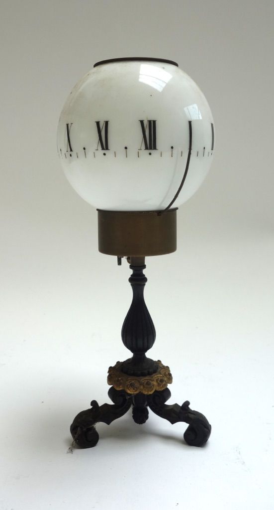 A candle clock, early 20th century, with opaque glass shade detailed with a band of Roman numerals over a triform bronze base, 24cm high.
