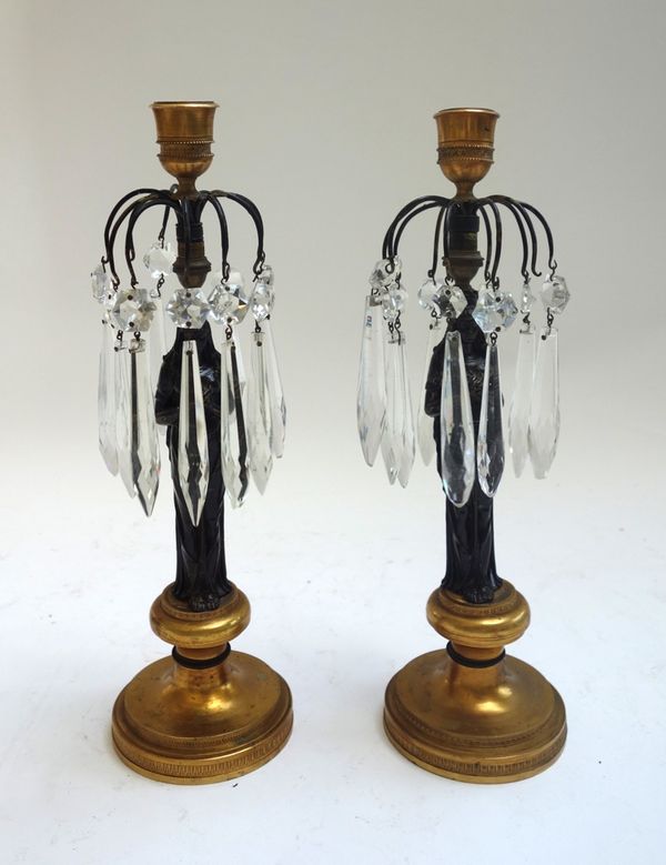 A pair of patinated and gilt bronze figural candlestick lustres, 19th century raised on a stepped circular foot, 33cm high, (2).