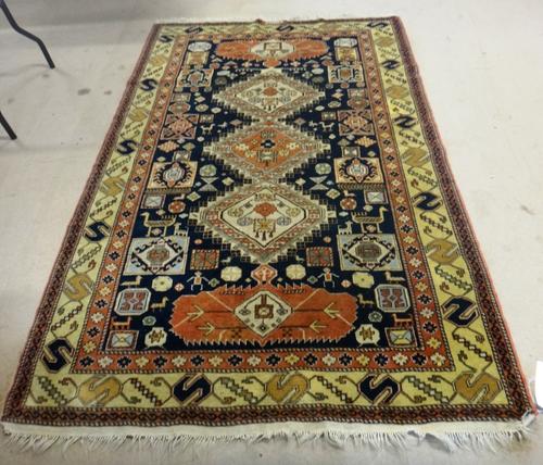 A Shirvan rug, Caucasian, the black field with three diamonds, stylised motifs, animals, birds, figures and beige border, 213cm x 140cm.