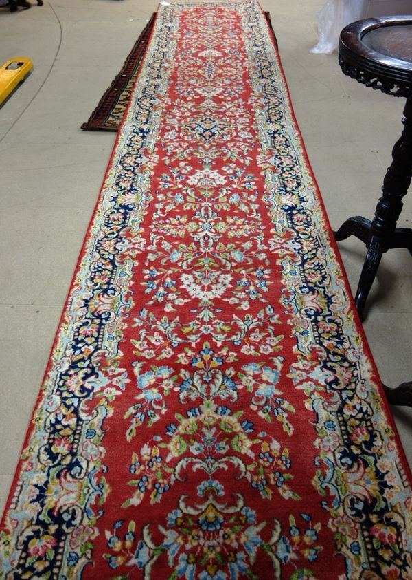 A Kerman runner, Persian, the dark pink field with floral sprays; a shaped black floral bolder, 575cm x 100cm.