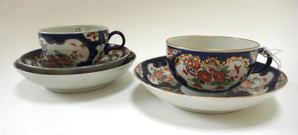Two Worcester porcelain tea cups and saucers, circa 1770, decorated with flowers against a gilt and blue scale ground, with blue painted marks, and a