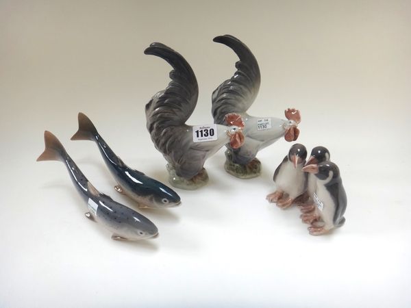 Five Royal Copenhagen animals; two cockerels 1025, a penguin group 1284 and two trout 2476, the first 19cm high. (5)