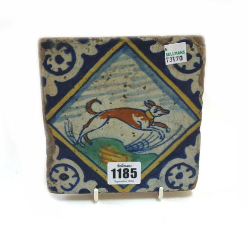 A Dutch Delft polychrome tile, early 17th century, painted with a leaping dog in a landscape, (a.f), 14cm.