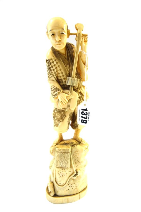 A Japanese marine ivory okimono of a musician, Meiji period, the man standing on a rocky mound playing a samisen, signed, 28cm. high.