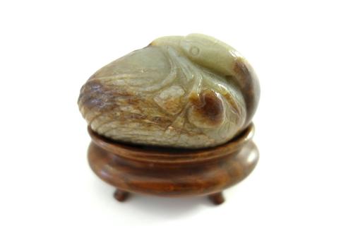 A Chinese celadon and russet jade bird, probably 17th century, carved with its head turned across its body and holding  a branch of fruiting peach in