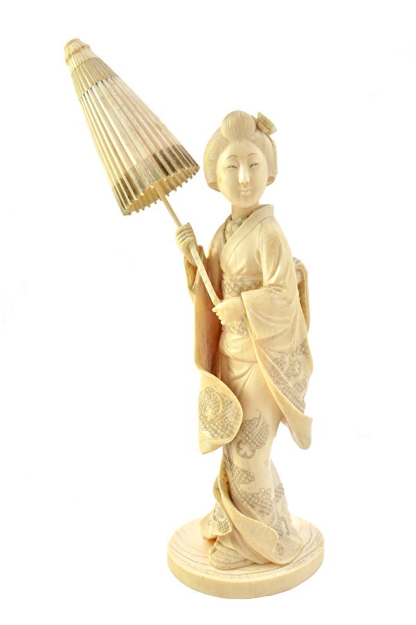 A Japanese ivory okimono of a bijin, Meiji period, carved standing in long robes and holding a parasol in both hands, signed, 28cm. overall height. Il