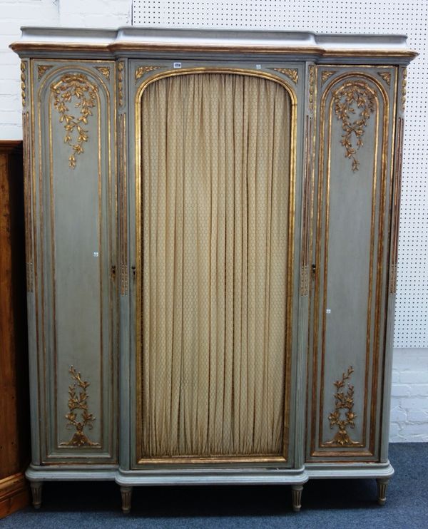 A Louis XVI style parcel gilt grey painted armoire, the breakfront central grill door flanked by smaller arch panel doors, on tapering turned fluted s