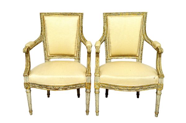 A pair of Louis XVI style parcel gilt off-white fauteuils, each with square back and semi-padded arms, over bow seats, on tapering fluted supports. (2