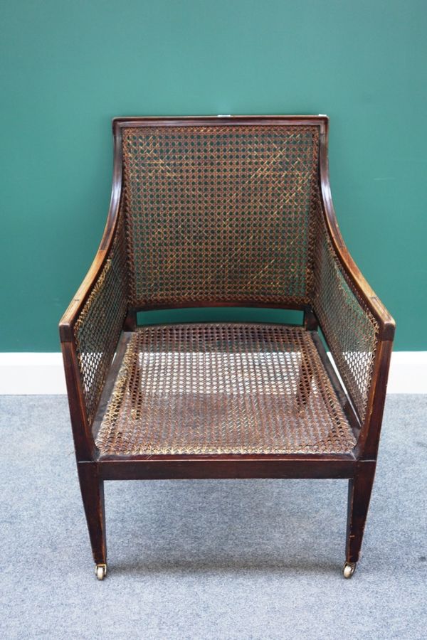 An early 19th century mahogany framed library bergère, with downswept arms and straight front seat on tapering square supports.