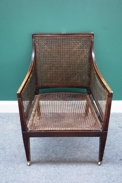 An early 19th century mahogany framed library bergère, with downswept arms and straight front seat on tapering square supports.