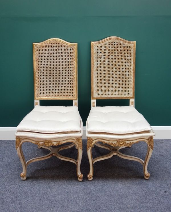 A pair of Louis XV style parcel gilt off-white painted side chairs, each with arched caned panelled back over serpentine seat, on cabriole supports un