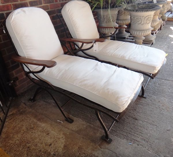 A pair of 20th century black painted iron reclining garden chairs, with loose cushions. (2)