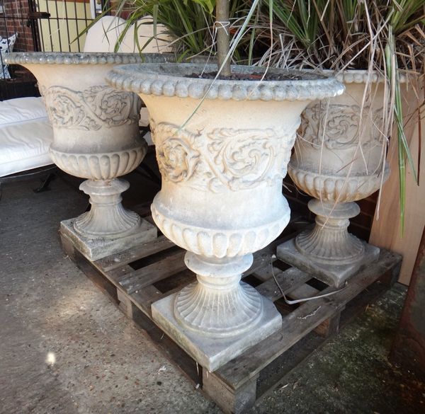 A set of four reconstituted stone campana shaped garden urns, on fluted socles, 56cm wide x 77cm high. (4)