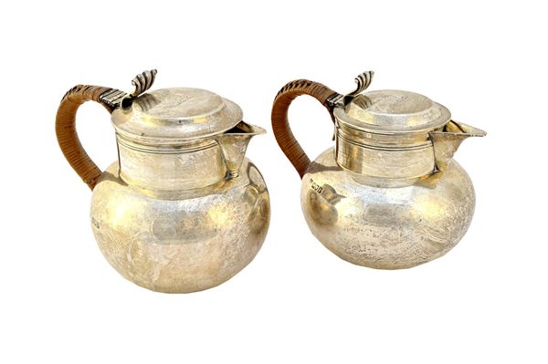 A pair of silver Jersey hinge lidded milk jugs, each with a fluted thumbpiece and with a rush woven handle, by Goldsmiths & Silversmiths Company Ltd,